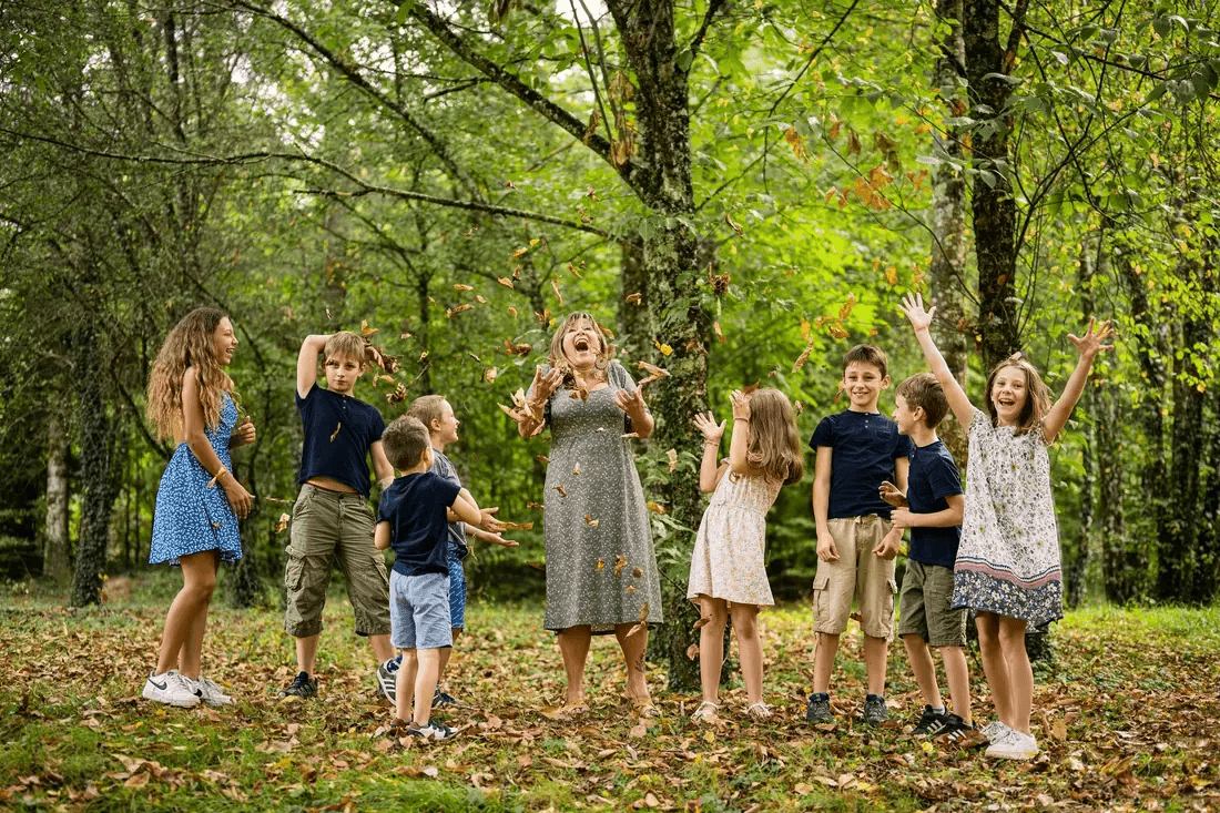 Groupe d'enfants et adulte jouant avec des feuilles d'automne en forêt – séance famille
