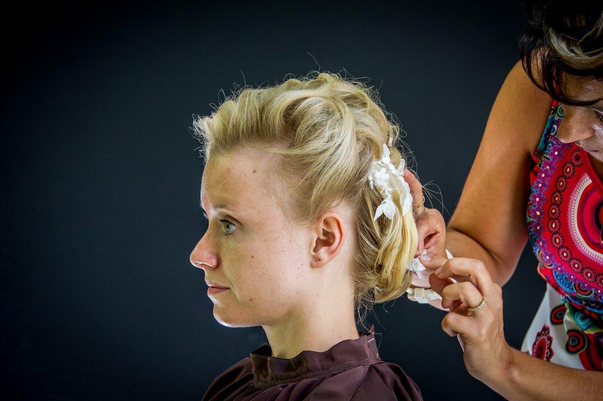 La mariée assise de profil, coiffeuse ajustant des fleurs blanches