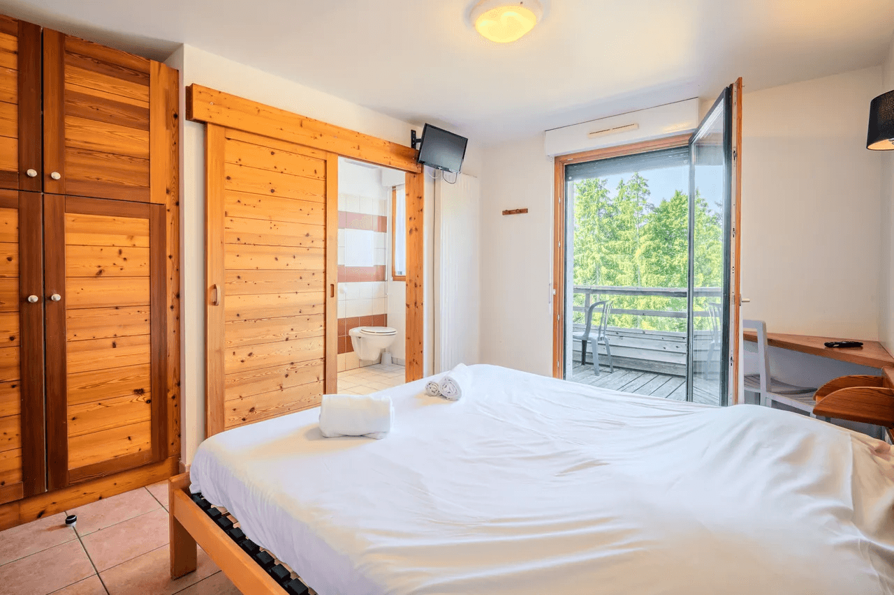 Chambre avec grande armoire en bois et porte-fenêtre sur terrasse