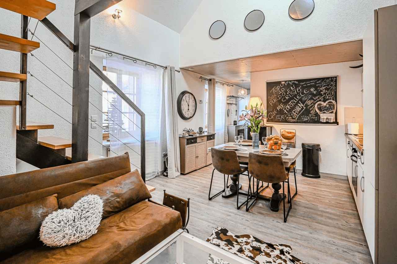 Séjour avec canapé en cuir, coin repas et escalier — intérieur chaleureux de gîte